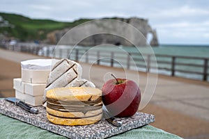 Cheeses of Normandy, round camembert cow cheese, yellow livarot, heartshaped neufchatel and view on alebaster cliffs Porte d`Aval