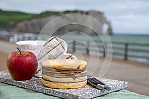 Cheeses of Normandy, round camembert cow cheese, yellow livarot, heartshaped neufchatel and view on alebaster cliffs Porte d`Aval