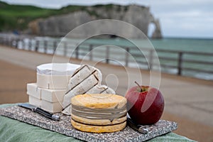 Cheeses of Normandy, round camembert cow cheese, yellow livarot, heartshaped neufchatel and view on alebaster cliffs Porte d`Aval