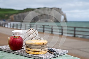 Cheeses of Normandy, round camembert cow cheese, yellow livarot, heartshaped neufchatel and view on alebaster cliffs Porte d`Aval