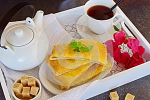 Cheesy pancakes with tea on a wooden tray.