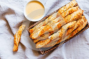 Cheesy puff pastry twists in a basket near a bowl of cheese sauce