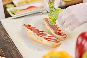 Chef adding lettuce on bun for hot dog.