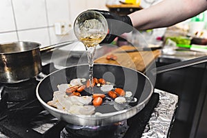 Chef adding white wine to the frying pan. Shrimps cooked with cherry tomatoes in white wine. Restaurant kitchen interior