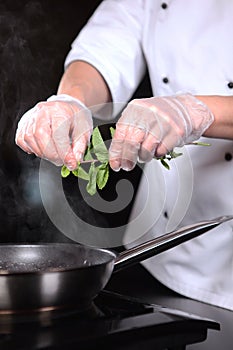 The chef adds mint leaves to the pan. Preparation of dishes. Unrecognizable vertical photo. Flaming of fruits and berries on fire