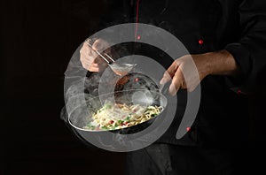 The chef adds spices to spaghetti in a steamed hot pan. Recipe or menu for restaurant or hotel on black background
