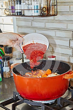 Chef adds tomato paste to the pot of ingredients on the gas stove