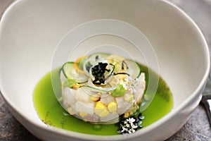 Chef assembles gourmet fish ceviche dish with corn, cucumber in green sauce