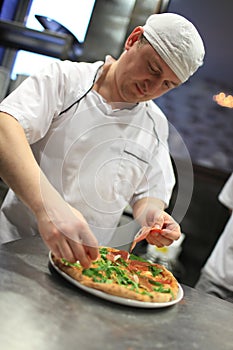 Chef baker in white uniform making pizza at kitchen