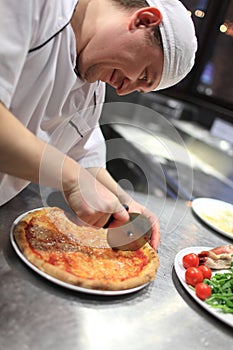 Chef baker in white uniform making pizza at kitchen