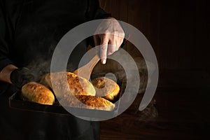 Chef bakes hot dog buns. Kitchen scraper in the cook hand. Space for advertising on a dark background