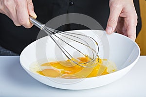 Chef beating eggs in a bowl witha a manual mixer