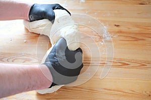 Chef in black gloves kneads dough for making bread, khinkali, dumplings and pastries. Male hands against a wooden table background