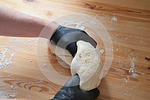 Chef in black gloves kneads dough for making bread, khinkali, dumplings and pastries. Male hands against a wooden table background
