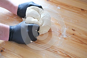 Chef in black gloves kneads dough for making bread, khinkali, dumplings and pastries. Male hands against a wooden table background