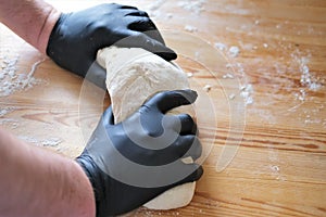 Chef in black gloves kneads dough for making bread, khinkali, dumplings and pastries. Male hands against a wooden table background