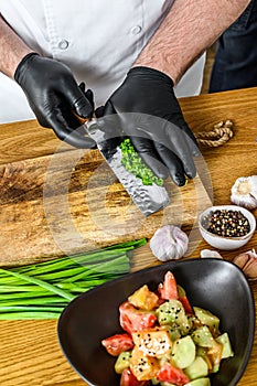 A chef in black gloves prepares a vegatarian vegetable salad. Concept of cooking healthy organic food