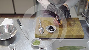 Chef in black rubber gloves preparing dish with raw tuna and salmon in modern restaurant kitchen close-up. Cook adding