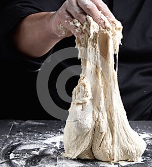 Chef in black uniform kneads white wheat flour dough