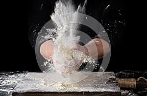 chef in black uniform sprinkles white wheat flour over the table