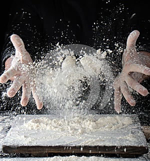 chef in black uniform sprinkles white wheat flour over the table