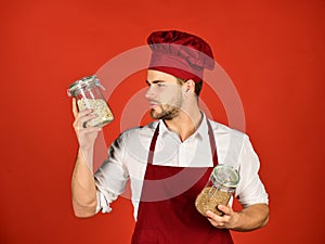 Chef in burgundy uniform holds jars with porridge.