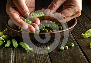 The chef cleans the pods of green peas. Work environment on the kitchen table. Cooking a dish of peas for lunch