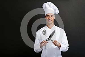 Chef cook against dark background smiling with hat holdinf spoon