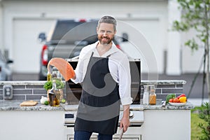 Chef in cook apron preparing salmon fish on barbecue grill outdoor. Man cooking tasty food on barbecue grill at backyard