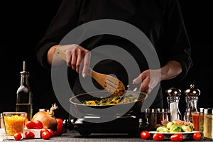 Chef cook. Frying a dish in a pan. Restaurant business, on a black background, horizontal photo. Ingredients, cafe or restaurant