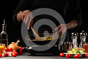 Chef cook. Frying a dish in a pan. Restaurant business, on a black background, horizontal photo. Ingredients, cafe or restaurant