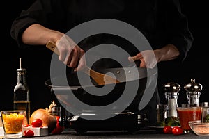 Chef cook. Frying a dish in a pan. Restaurant business, on a black background, horizontal photo. Ingredients, cafe or restaurant