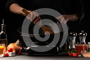 Chef cook. Frying a dish in a pan. Restaurant business, on a black background, horizontal photo. Ingredients, cafe or restaurant
