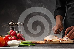 Chef cook prepares fresh chicken with vegetables. Against the background of a gray wall. Recipe book. Culinary and gastronomy,