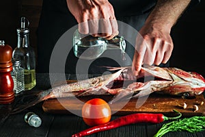 Chef or cook prepares fresh fish bighead carp with add vinegar. Preparation for cooking herring. Working environment in the photo