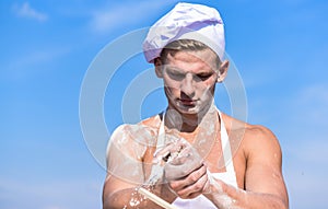 Chef cook preparing dough for baking with flour. Man on busy face wears cooking hat and apron, sky on background. Baker