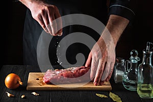 Chef or cook sprinkles the raw beef meat with salt. Preparing meat before baking. Working environment in kitchen of restaurant or