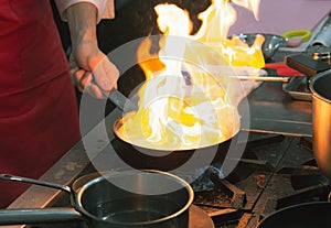 Chef cooking with flame in a frying pan on a kitchen stove