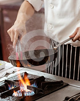 Chef cooking with flame in a frying pan on a kitchen stove