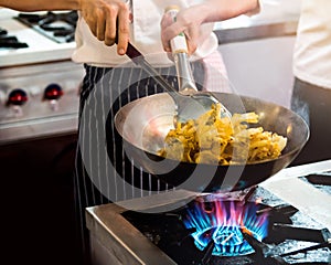 Chef cooking with flame in a frying pan on a kitchen stove