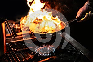 Chef cooking with flame in a frying pan on a kitchen stove