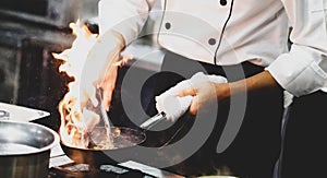 Chef cooking with flame in a frying pan on a kitchen stove, Chef in restaurant kitchen at stove with pan, doing flambe on food