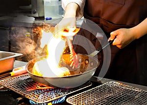 Chef cooking with flame in a frying pan on a kitchen stove, Chef in restaurant kitchen at stove with pan, doing flambe on food