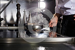 Chef cooking in frying pan on kitchen stove, cropped