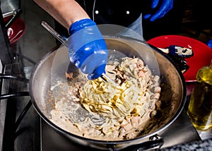 Chef cooking pasta with mussels in pan. Italian style cuisine. Restaurant.