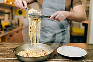 Chef cooking pasta, pan on wooden kitchen table