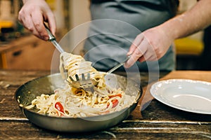 Chef cooking pasta, pan on wooden kitchen table