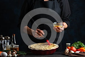 Chef cooking pie. Grease a pie with eggs for good result. Delicious meal for everyone. Restaurant recipe. Dark background