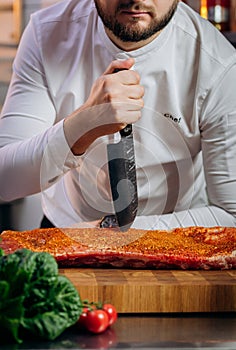 Chef cooking raw meat in the kitchen. chef holds a professional kitchen knife. Concept of Cooking process and preparing dishes