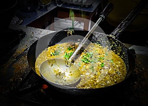 A chef cooking tadka fry in a frying pan at a road side food corner on a stove over flames